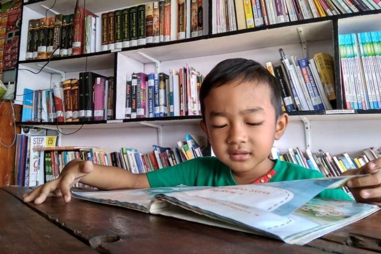 Ilustrasi seorang anak sedang membaca buku di sebuah perpustakaan desa. Foto: KOMPAS.COM/MASRIADI SAMBO