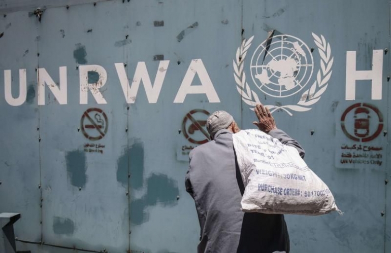 Seorang pria Palestina membawa tas di depan lambang United Nations Relief and Works Agency for Palestine Refugees (UNRWA) di luar kantor badan tersebut di Kota Gaza. (AFP)