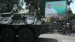 Panser TNI melintas di depan baliho yang akan dicopot (detik.com).