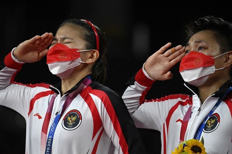 Pasangan ganda putri Indonesia Greysia Polii (kiri) dan Apriyani Rahayu (kanan) memberi hormat dengan medali emas bulu tangkis ganda putri pada upacara Olimpiade Tokyo 2020 di Musashino Forest Sports Plaza di Tokyo pada 2 Agustus 2021. (Foto: AFP/ALEXANDER NEMENOV via Kompas.com)