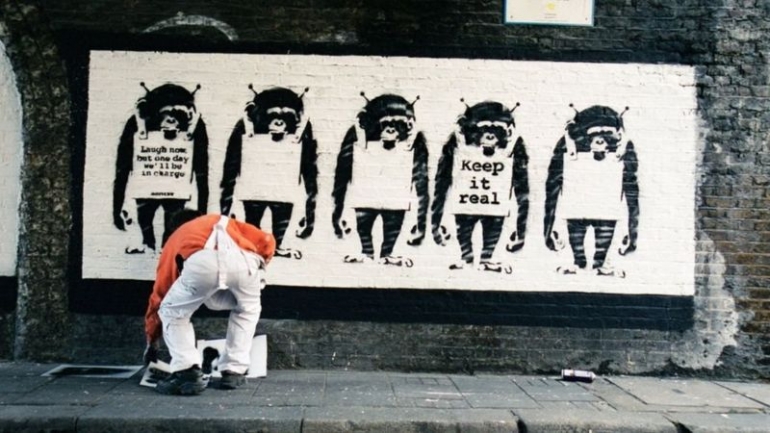Potret Banksy saat sedang membuat sebuah stensil di Bristol, Inggris. | Steve Lazardies via BBC.com