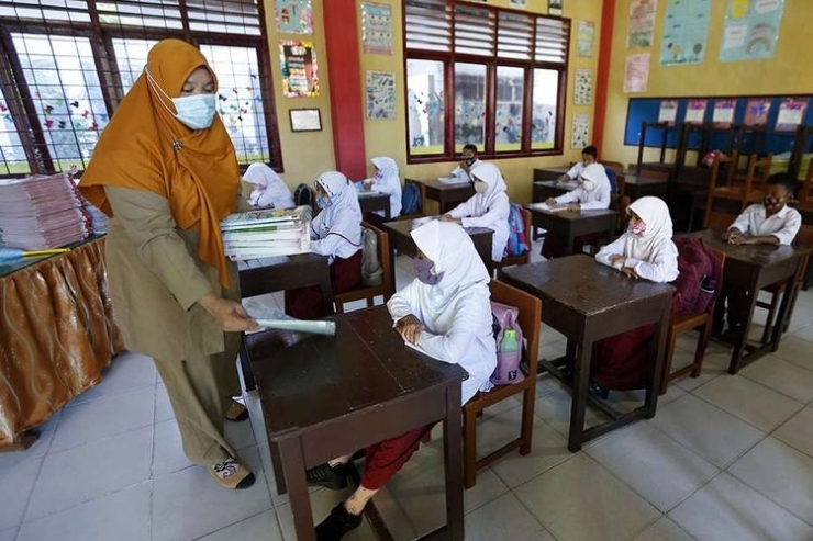 Guru membagikan buku pelajaran kepada pelajar pada hari pertama sekolah tatap muka di SD Negeri 42, Banda Aceh, Aceh, Senin (4/1/2021).| Sumber: ANTARA FOTO/IRWANSYAH PUTRA