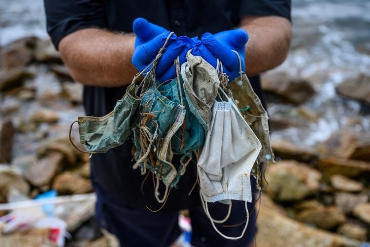 ilustrasi memegang sampah masker sekali pakai yang berserakan di Discovery Bay di Pulau Lantu yang terpencil di Hong Kong.(Foto: AFP/ANTHONY WALLACE via kompas.com)