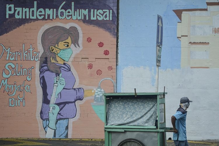 Seorang pedagang menarik gerobaknya dengan latar belakang mural imbauan 'Pandemi Belum Usai di Jakarta, Minggu (18/7/2021). (ANTARA FOTO/M RISYAL HIDAYAT via kompas.com)