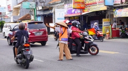 Aksi Bu Paiyem sosok Pak Ogah wanita saat sedang mengatur lalu lintas di pertigaan Jalan Wates yang mengarah ke Jalan Nitipuran (foto oleh Firna).