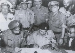 Lt. Jen. Niazi dari Pakistan menandatangani dokumen penyerahan tentaranya kepada Pasukan India dan pejuang Bangladesh. | Sumber: Angkatan Laut India