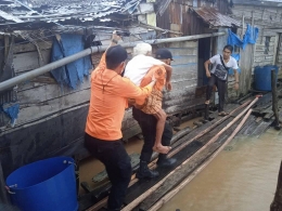 Petugas BPBD Indragiri Hilir mengevakuasi Kakek Husein dari rumahnya yang kebanjiran. (Foto : FB grup Poros Kebijakan Indragiri Hilir)