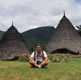 Foto Alexander bersama dengan background rumah adat (sumber: dokumen pribadi)