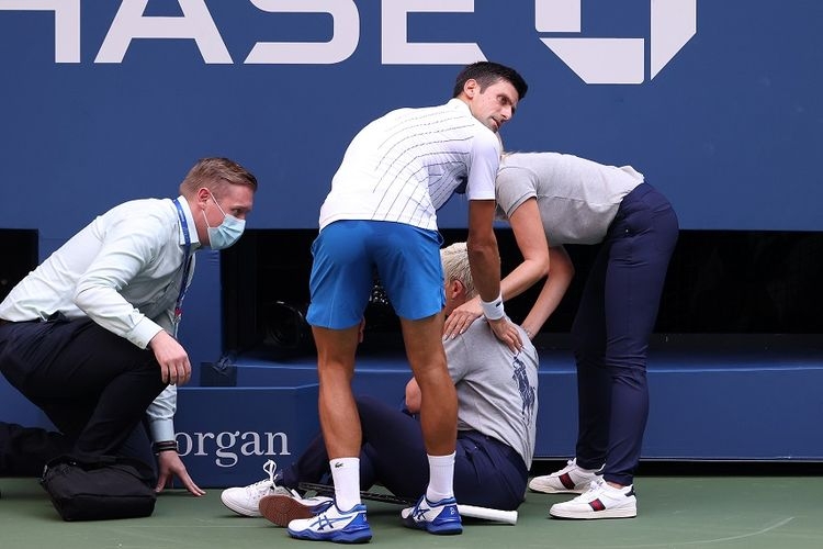 Petenis Novak Djokovic (celana biru) dan hakim garis (duduk) yang terkena pukulan bola dalam laga keempat saat melawan Pablo Carreno Busta dari Spanyol pada US Open 2020 di USTA Billie Jean King National Tennis Center pada 6 September 2020. (AFP/AL BELLO via kompas.com)