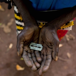 Seorang perempuan di Mombasa, Kenya, menunjukkan pisau silet yang ia gunakan untuk melakukan sunat perempuan | Foto milik Ivan Lieman/Barcroft Media