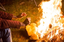 Young man warming up his hands above the bonfire. Sumber: freepik.com