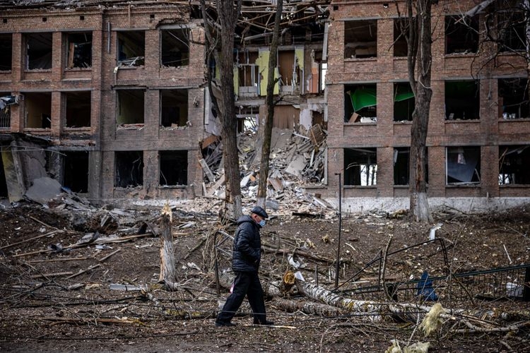 Seorang pria berjalan di depan sebuah bangunan yang hancur setelah serangan rudal Rusia di kota Vasylkiv, dekat Kyiv, Minggu (27/2/2022). (Foto: AFP/DIMITAR DILKOFF via kompas.com)