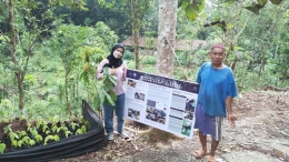 Windi, mahasiswa Tim KKN-PPM UGM Subunit Nglanggeran Kulon (kiri) menyerahkan dan memasang infografis bilingual bersama Pak Sutoyo (kanan). 