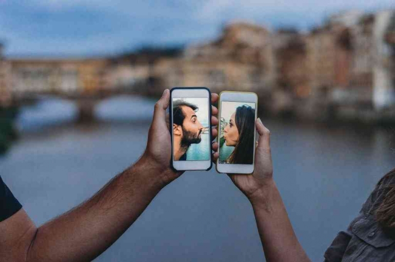 Ilustrasi gambar Bidikan konseptual pasangan dewasa muda berciuman melalui ponsel. Sumber foto: IStock/FilippoBacci