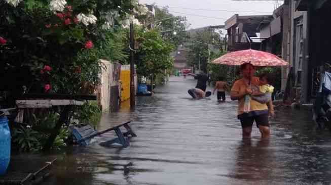 (25/2/2021) Seorang ibu tengah mengendong bayinya berjalan dalam genangan air  [Semarangpos.com/BPBD Kota Semarang ]