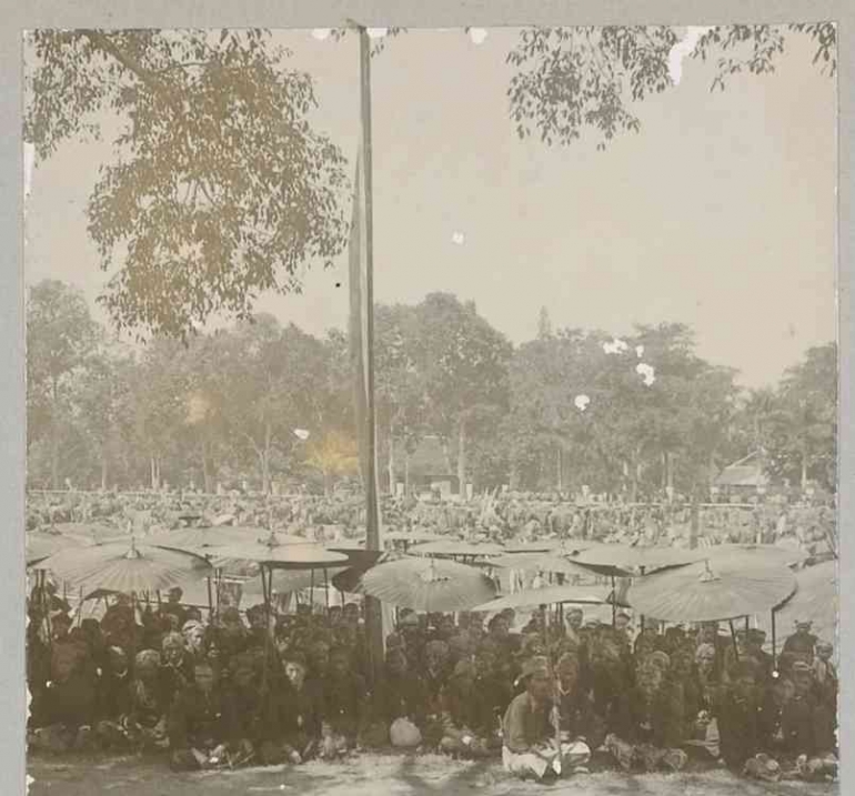 Pengunjung berpakaian adat berteduh dengan payung. Sumber: Digital Collection Leiden University Libraries