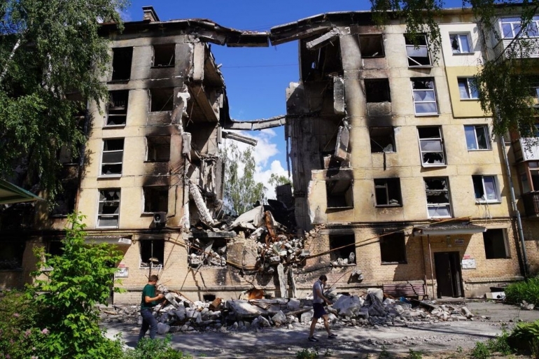 Warga melintasi gedung yang hancur dihajar rudal di wilayah Gostomel, Provinsi Kyiv, Ukraina, Sabtu (18/6/2022). Gedung ini berada di sekitar pangkalan udara Gostomel yang merupakan salah satu lokasi yang pertama kali diserang Rusia. (Foto: KOMPAS/HARRY SUSILO)