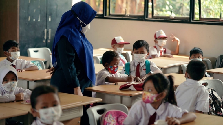 Guru memperhatikan pekerjaan anak didik dalam pembelajaran tatap muka (PTM) di SDN Klender 01, Jakarta Timur, Selasa (4/1/2022).| Dok KOMPAS/AGUS SUSANTO
