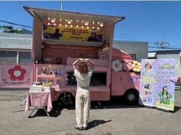 Sejeong di depan truk makanan. Banner sebelah kanan itu ada tulisan SEMANGAT dan Kami Cinta Kamu (Instagram @clean_0828)