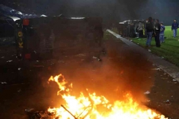 Petugas berpakaian preman berdiri di dekat reruntuhan kendaraan polisi yang rusak selama bentrokan. (AP: Yudha Prabowo) via ABC