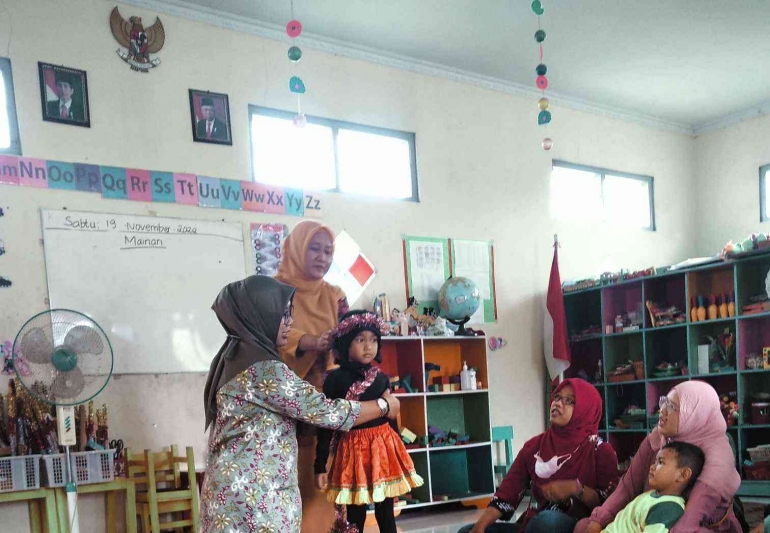 Ibu guru sedang memasang hiasan pada penutup kepala murid di TK Pertiwi 28 Bantul. Foto wahyuTanoto