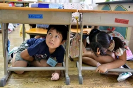 Anak-anak sekolah dasar berlindung di bawah meja mereka saat latihan gempa di sebuah sekolah di Tokyo. (AFP PHOTO/YOSHIKAZU TSUNO via Kompas.com)