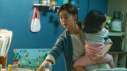Kim Jiyoung menyiapkan makan malam sembari menggendong anaknya (sumber: Cultura Magazine)