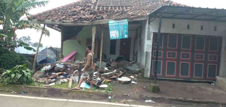 SEORANG WARGA berjalan di depan rumah yang hancur berlokasi di Kampung Lebaksaat, Desa Cirumput. (Foto: Dede Aripin).