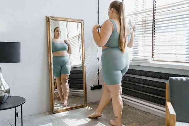 seorang remaja perempuan memandangi tubuhnya di depan cermin-photo by mart production from pexels