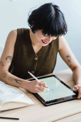 https://www.pexels.com/photo/smiling-woman-drawing-on-graphic-tablet-with-pencil-at-table-7147701/