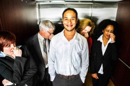 Seorang pemuda tersenyum malu (atau bangga) di lift sementara orang memegang hidung mereka (istockphoto.com)