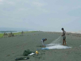 Seorang nelayan dibantu anaknya membetulkan jaring yang terkena sampah. | Dokumentasi pribadi