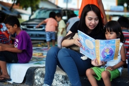 Seorang relawan dari Komunitas Tanah Ombak sedang mengajar membaca kepada anak-anak di kawasan Sebrang Pabayan, tepi Sungai Batang Arau, Padang, Sumatera Barat, Minggu (16/7/2017). (KOMPAS.com / RAMDHAN TRIYADI BEMPAH)