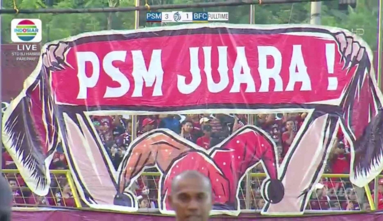 Spanduk raksasa bertuliskan PSM JUARA menghiasi laga PSM vs Bhayangkara. Sumber foto: live streaming Indosiar.