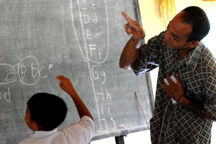 Guru mengajar menggunakan bahasa isyarat kepada seorang murid tunarungu di Sekolah Dasar, di Desa Bengkala, Singaraja, Bali, 20 Juli 2016. Desa Bengkala telah menjadi rumah bagi sejumlah besar penyandang tunarungu turun temurun.(AFP PHOTO / SONNY TUMBELAKA via KOMPAS.com) 