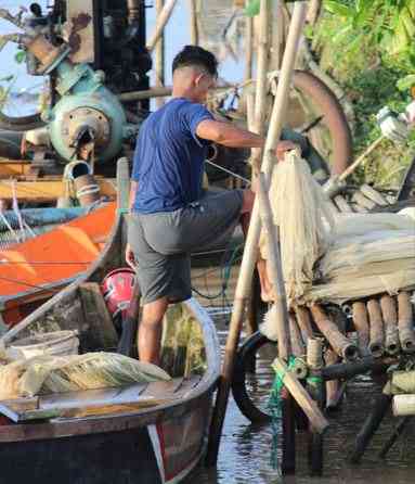 Seorang nelayan sedang mengeluarkan jala dari perahu untuk memeriksa hasil tangkapannya