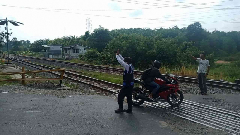 Tampak petugas perlintasan kereta api Tebing Bantaian memberi aba-aba kepada pengendara untuk berhenti | Sumeks.disway.id (2/10/2022)
