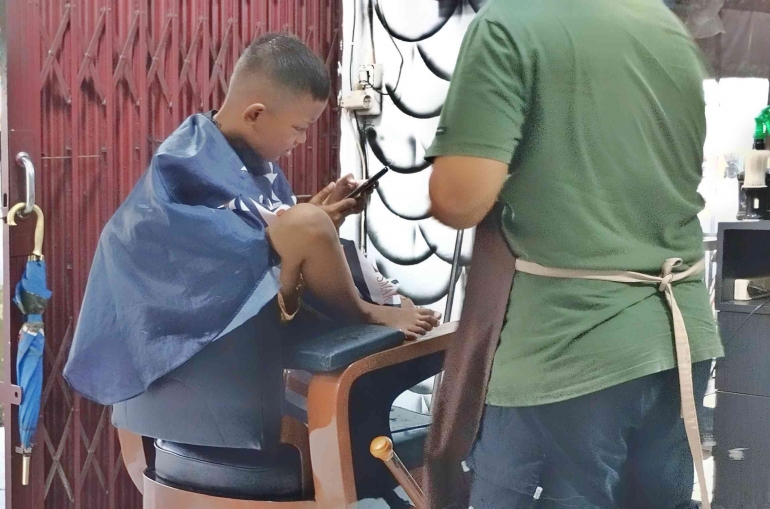 Seorang anak yang diantar orangtuanya untuk melakukan pangkas rambut. (foto Akbar Pitopang)