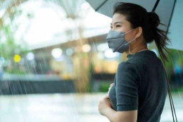 Ilustrasi seorang wanita memakai masker dan menggunakan payung di tengah hujan (sumber:freepik)