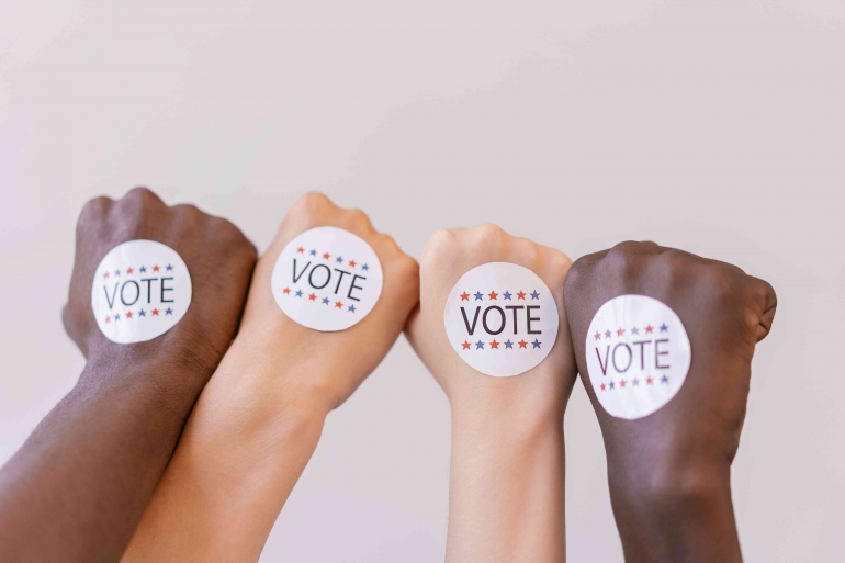 Sumber gambar: https://www.pexels.com/photo/close-up-photo-of-vote-stickers-on-people-s-fist-8846632/