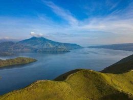 Danau Toba dengan latar depan Bukit Holbung dan latar belakang Gunung Pusukbuhit (Foto: calderatobageopark.org) 