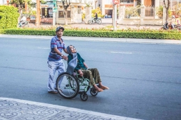 Pria mendorong seorang wanita duduk di kursi roda, Foto: Pexels.com/Streetwindy 