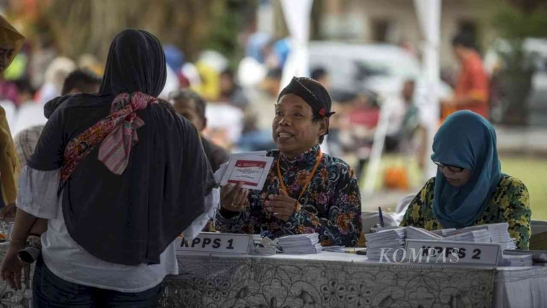 Petugas KPPS memberikan surat suara kepada warga. (KOMPAS/FERGANATA INDRA RIATMOKO)