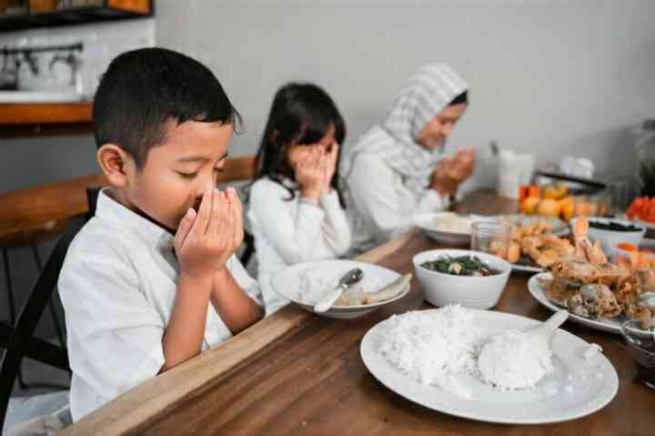 Ilustrasi seorang anak laki-laki bersama keluarga di rumah sedang berdoa menjelang berbuka puasa. (Sumber : Freepik)