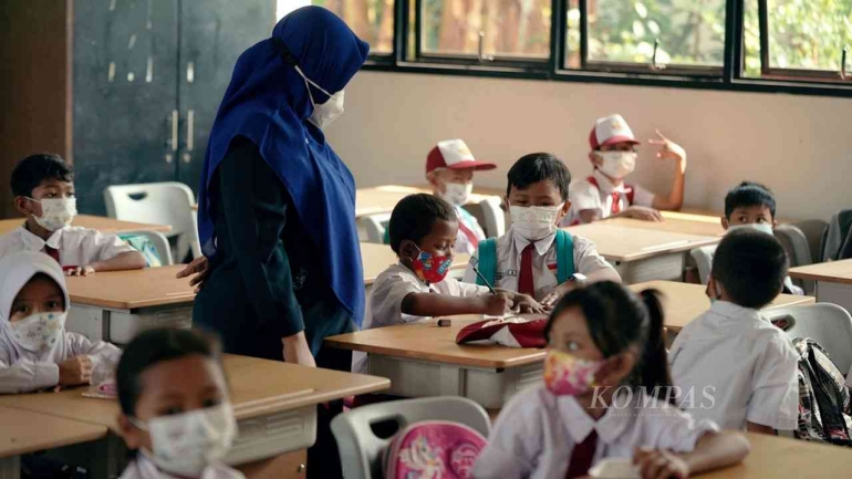 Guru memperhatikan pekerjaan anak didik dalam pembelajaran tatap muka (PTM) di SDN Klender 01, Jakarta Timur (KOMPAS/AGUS SUSANTO)