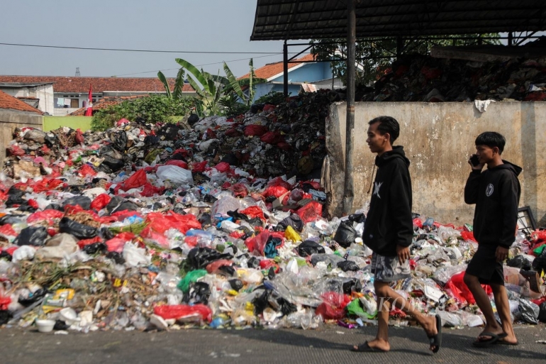 Dua remaja berjalan di samping tumpukan sampah di Jalan Naming D Bothin, Kota Depok, Jawa Barat, Jumat (28/7/2023). (KOMPAS/FAKHRI FADLURROHMAN)