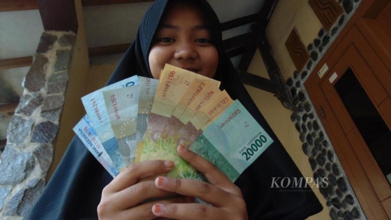 ilustrasi: Tersenyum menunjukkan uang THR (tunjangan hari raya) yang didapatkan saat Lebaran. (Foto: KOMPAS/ABDULLAH FIKRI ASHRI)