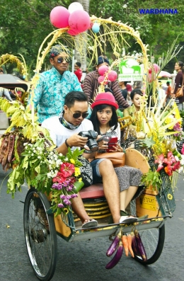 Sepasang wisatawan di atas becak penuh bunga dan hiasan.