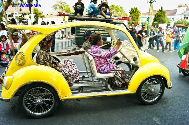 Anak-anak berpakaian adat Jawa menaiki sepeda modifikasi berbentuk mobil.